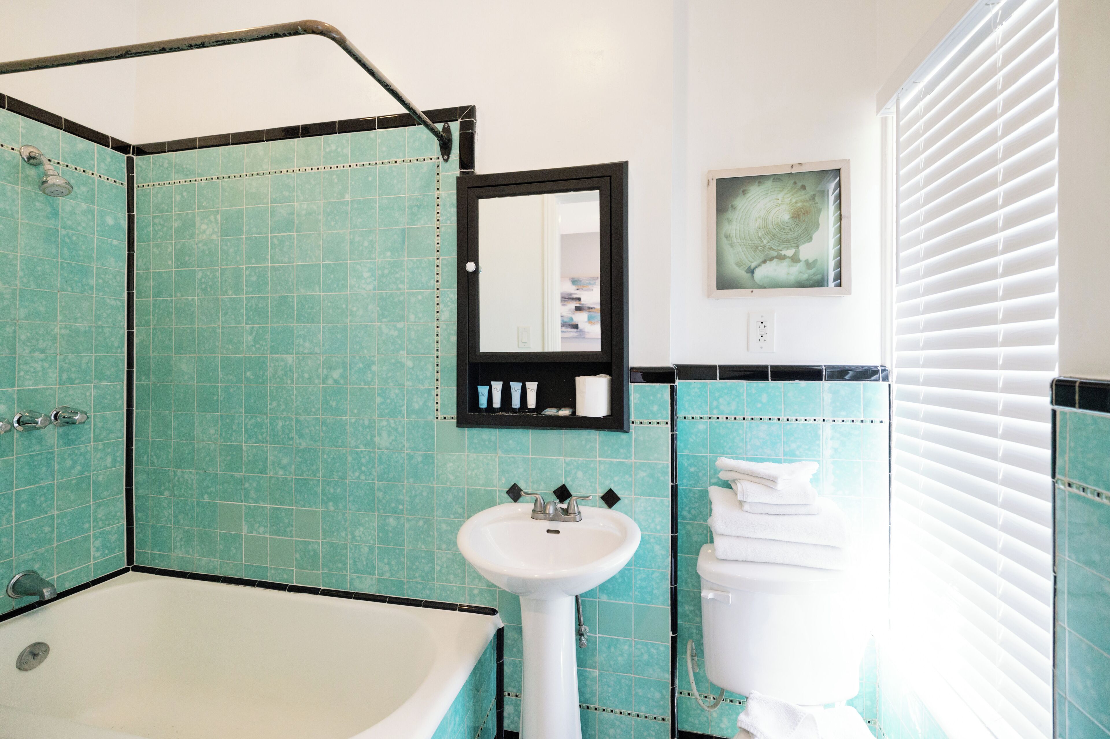 Un baño con bañera, lavamanos e inodoro, con azulejos verde mar y un espejo en marco.