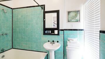 Un baño con bañera, lavamanos e inodoro, con azulejos verde mar y un espejo en marco.