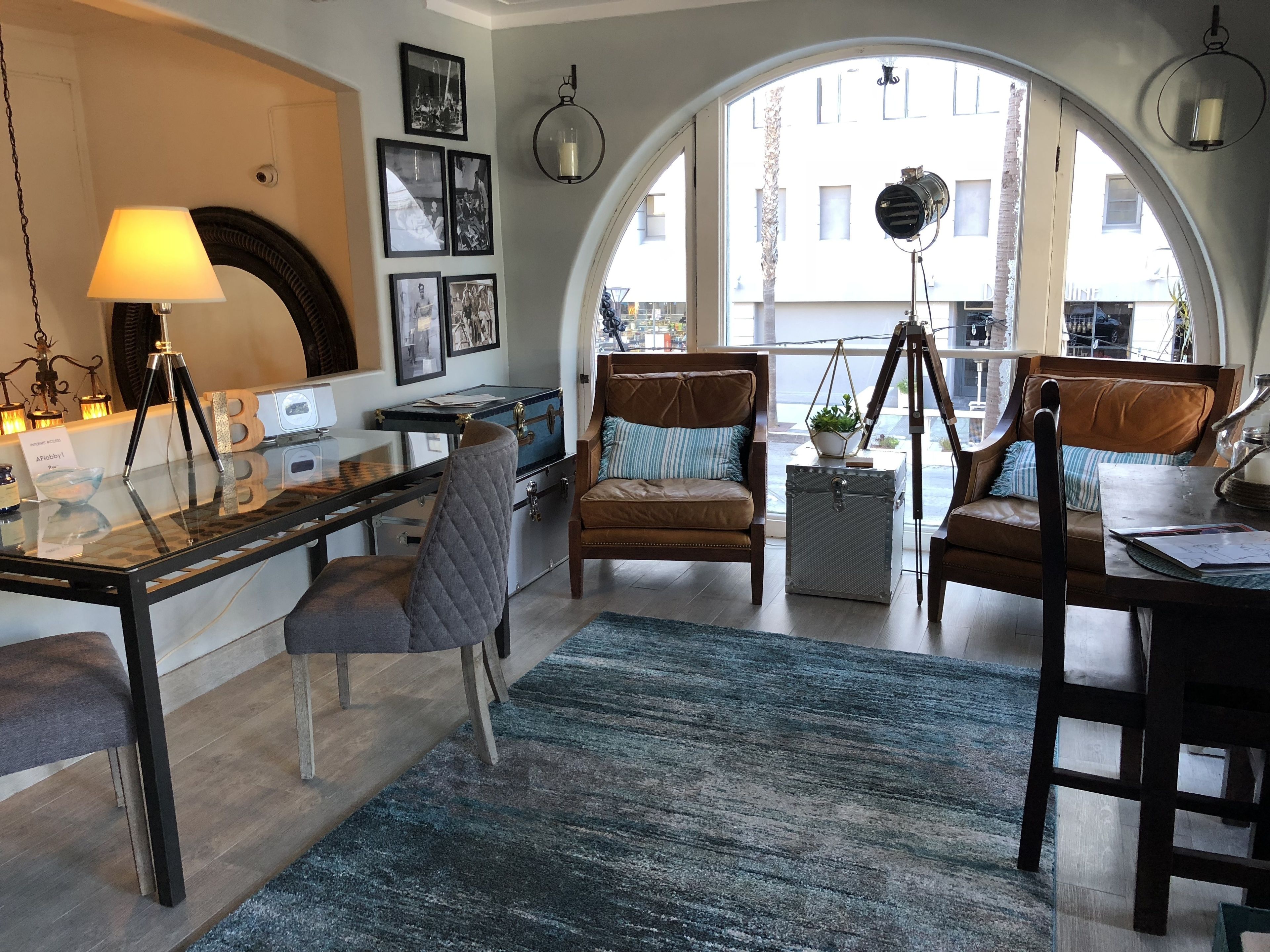 A cozy living room with a glass table, leather chairs, a tripod, and a large arched window overlooking a building.