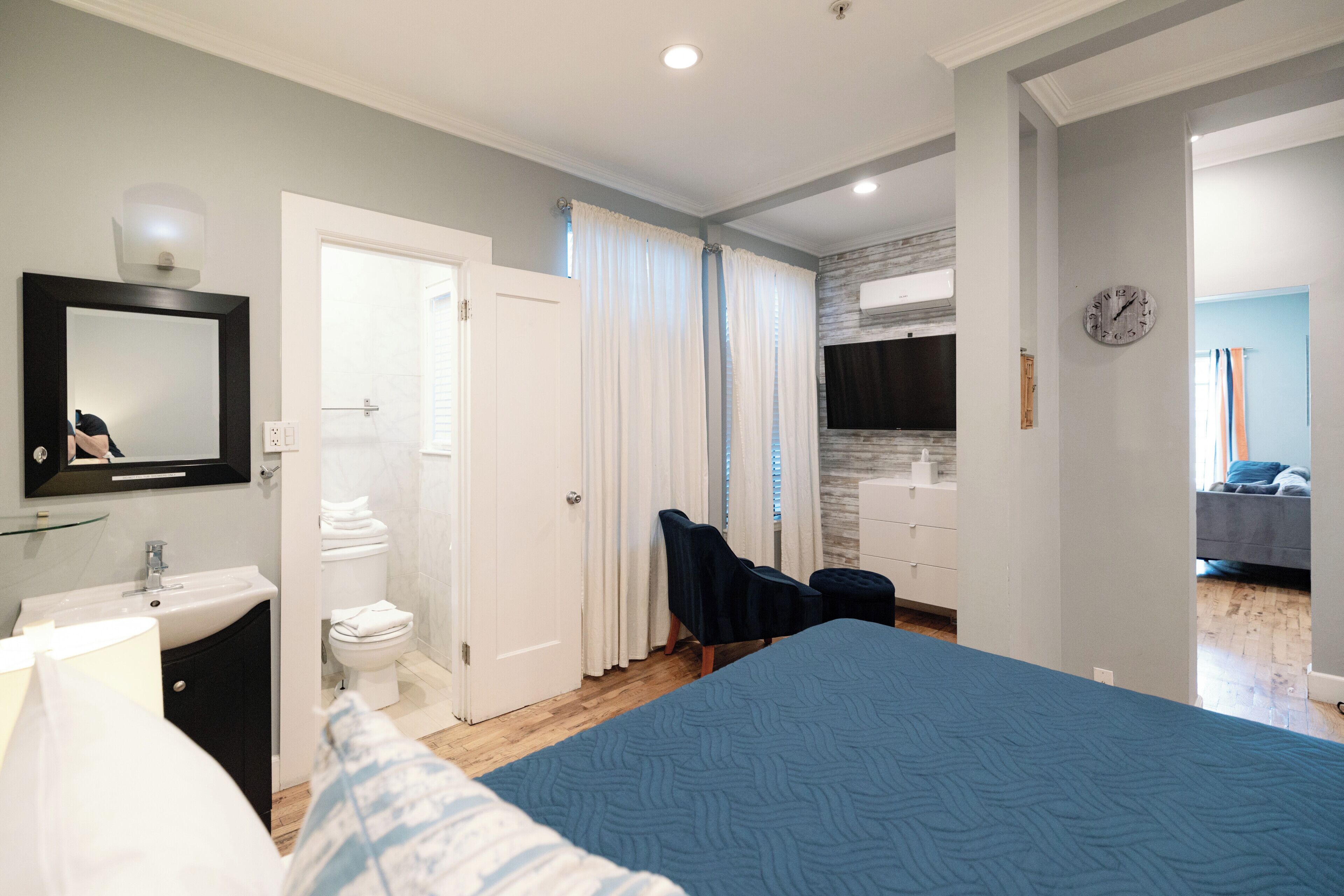 A modern bedroom with a large bed, a bathroom with a toilet and sink, and a view of the living area.