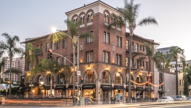 A multi-story building with arched windows and a brick facade, featuring several ground-level commercial spaces with signage.