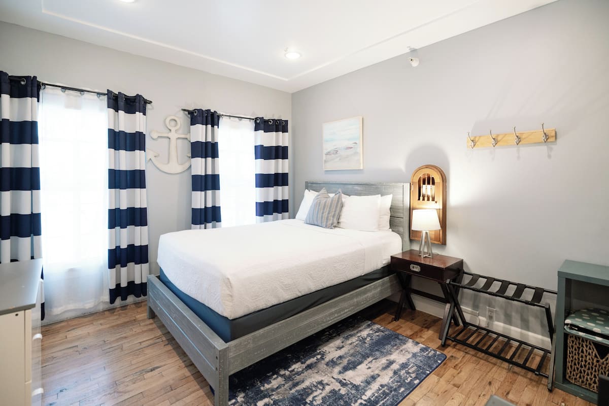 Une chambre à coucher avec un lit, des rideaux, une table de chevet, une lampe et une étagère fixée au mur.