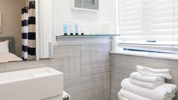 A modern bathroom with a white sink, a toilet with stacked towels, a starfish decoration, and a window with blinds.