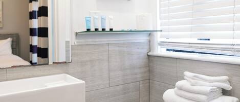 A modern bathroom with a white sink, a toilet with stacked towels, a starfish decoration, and a window with blinds.