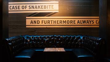 Una habitación con poca luz, con un banco de cuero negro, una mesa y una pared con un letrero que dice 'CASE OF SNAKEBITE AND FURTHERMORE ALWAYS CA'.