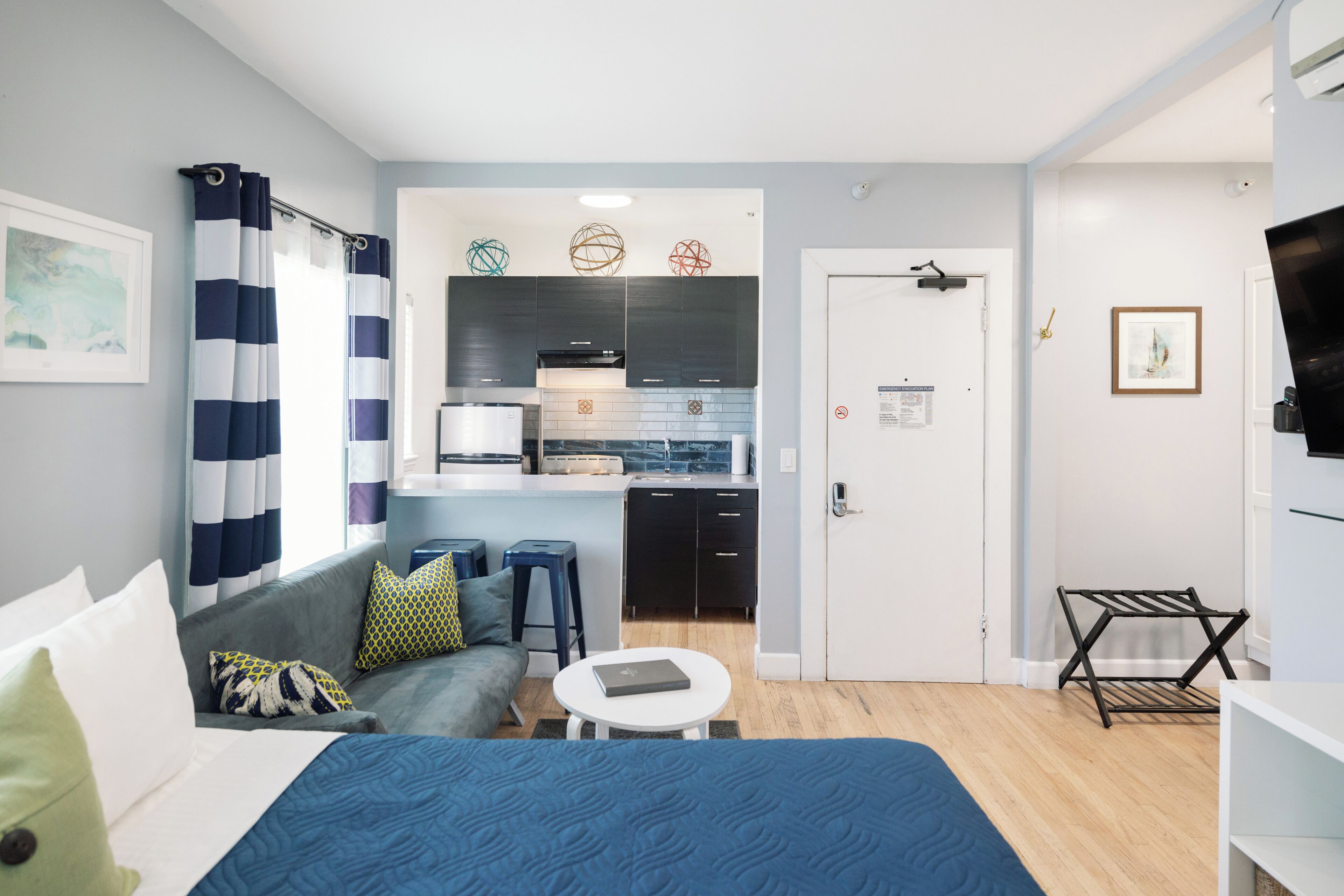 Una habitación de hotel moderna con una cama, una mesita redonda pequeña, un sofá, una kitchenette y un televisor.
