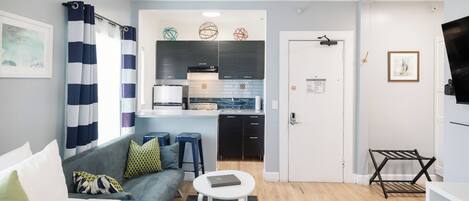Una habitación de hotel moderna con una cama, una mesita redonda pequeña, un sofá, una kitchenette y un televisor.