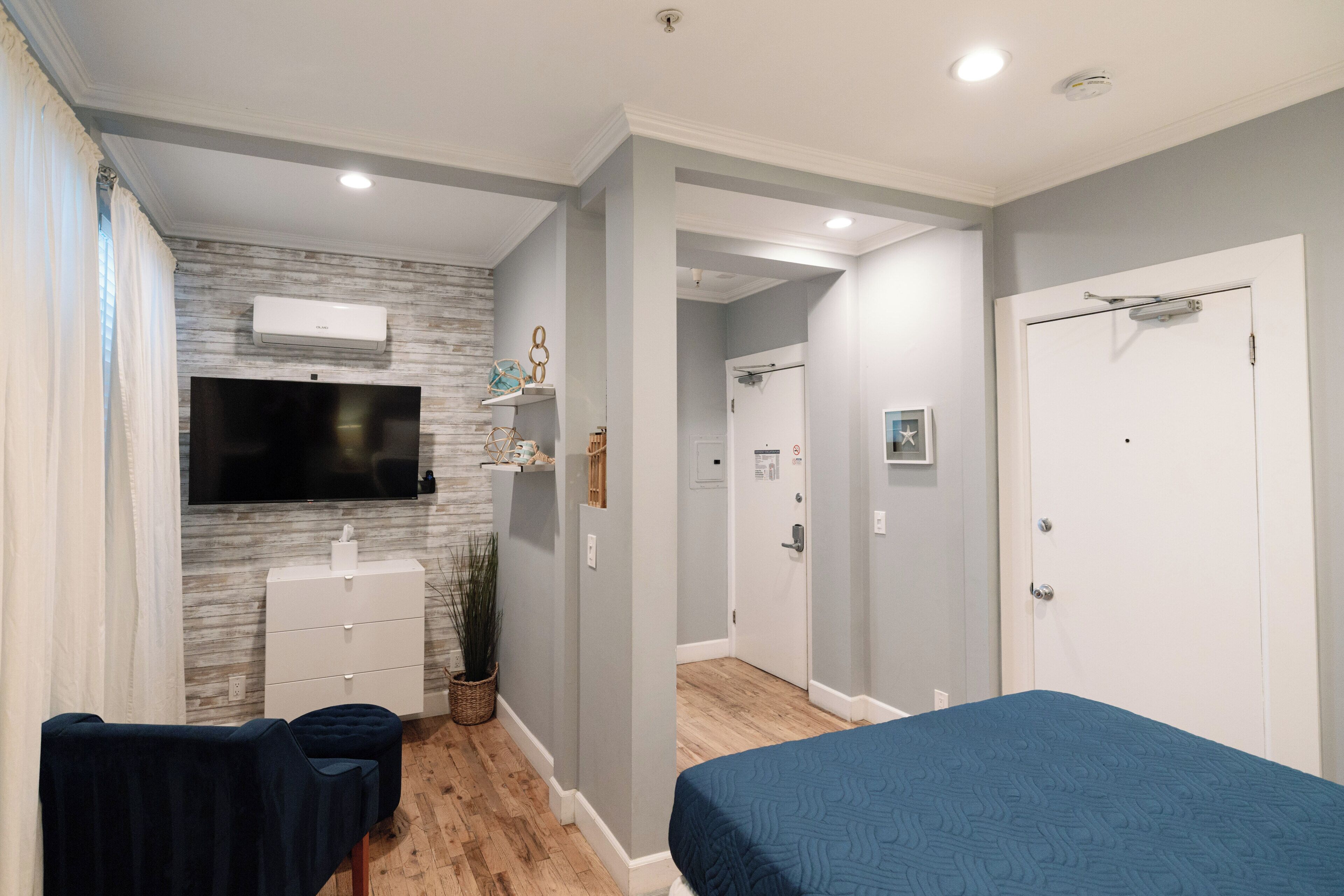 Une chambre à coucher comprenant un lit, un téléviseur fixé au mur, une commode et un petit coin salon.