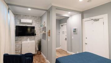 Une chambre à coucher comprenant un lit, un téléviseur fixé au mur, une commode et un petit coin salon.