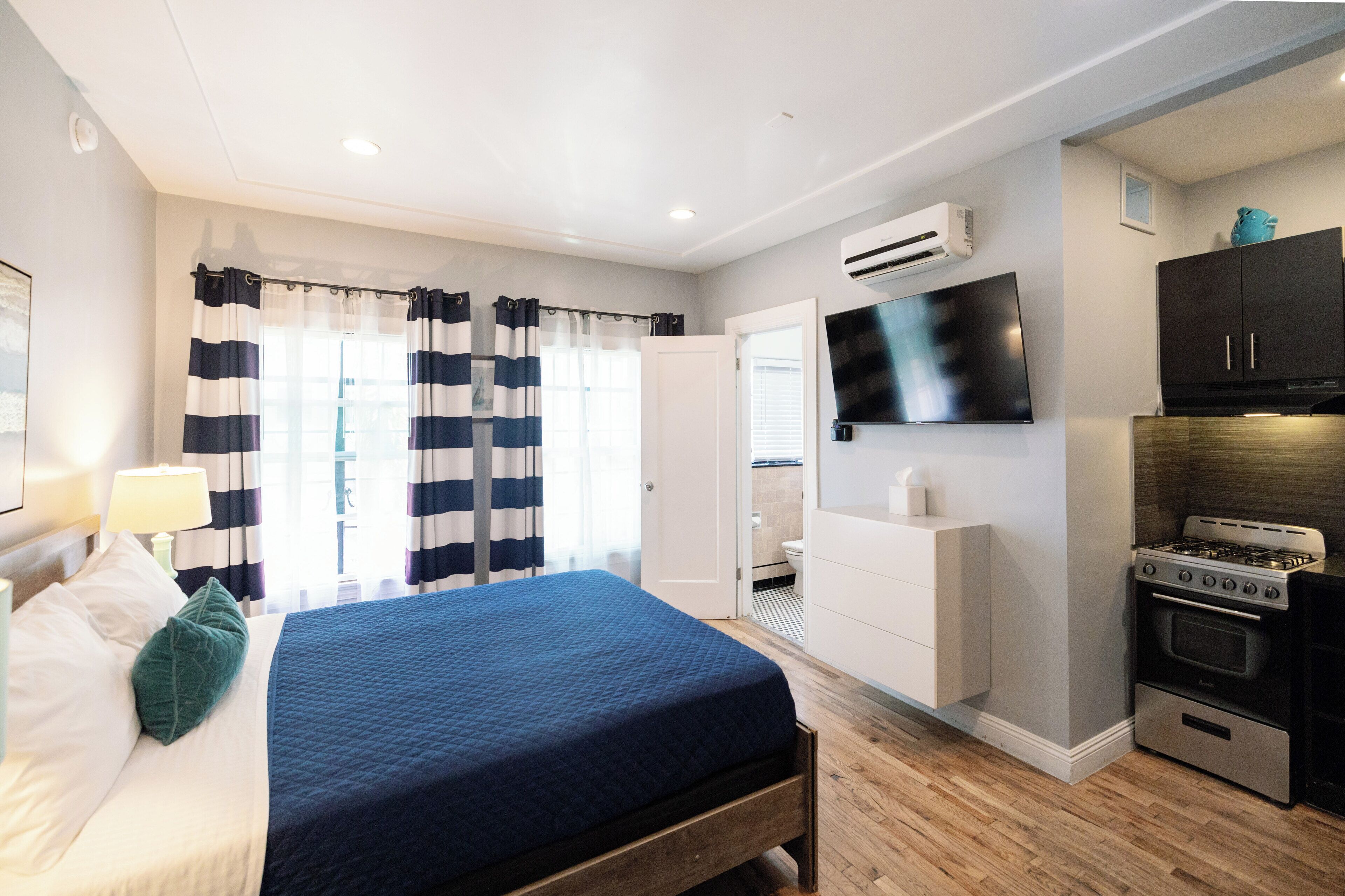 Un dormitorio con cama, televisión, kitchenette y baño.