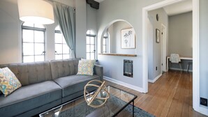 A modern living room with a grey sofa, a glass coffee table, and a large window with curtains.