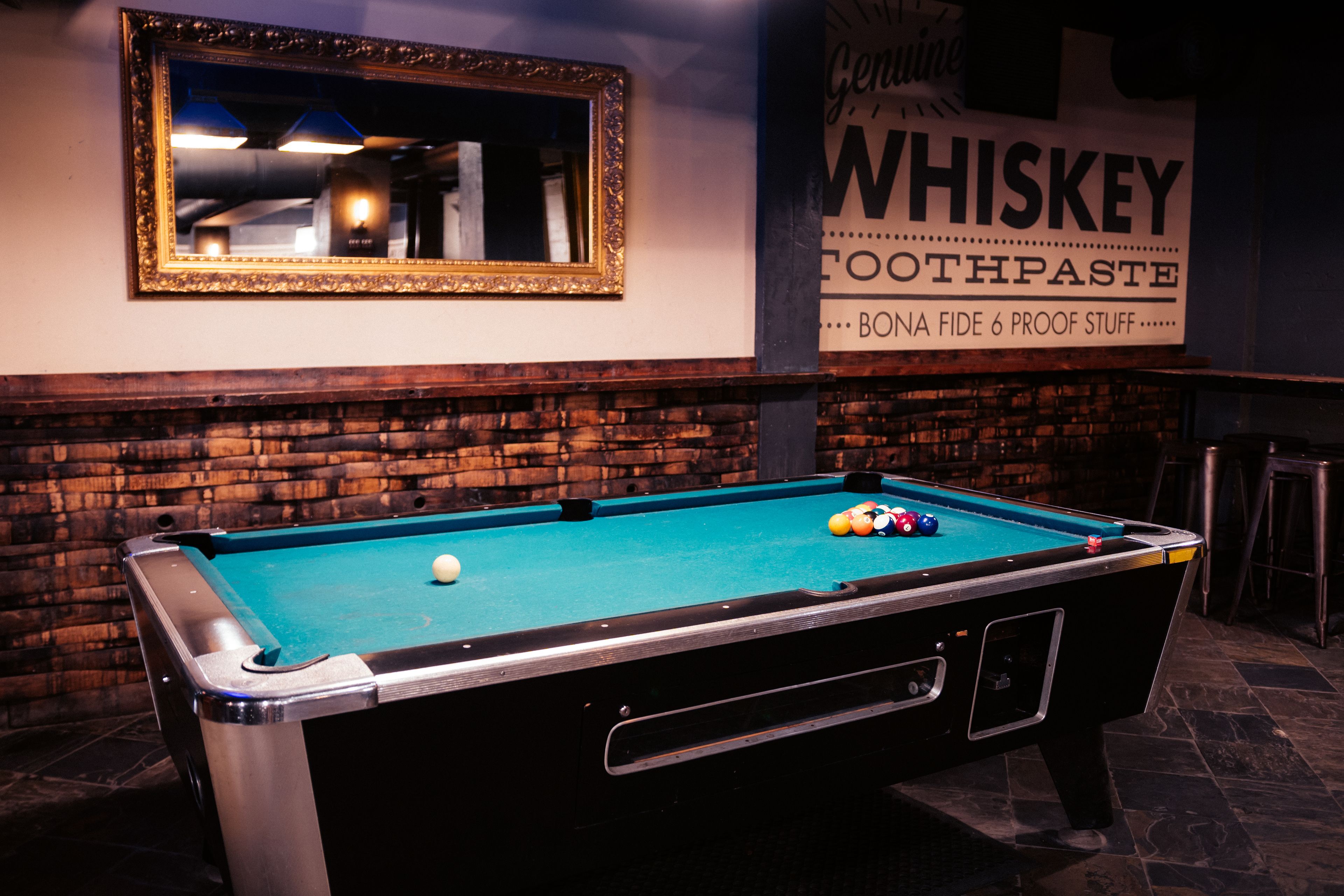 A pool table with balls, a mirror, and a sign advertising whiskey toothpaste.