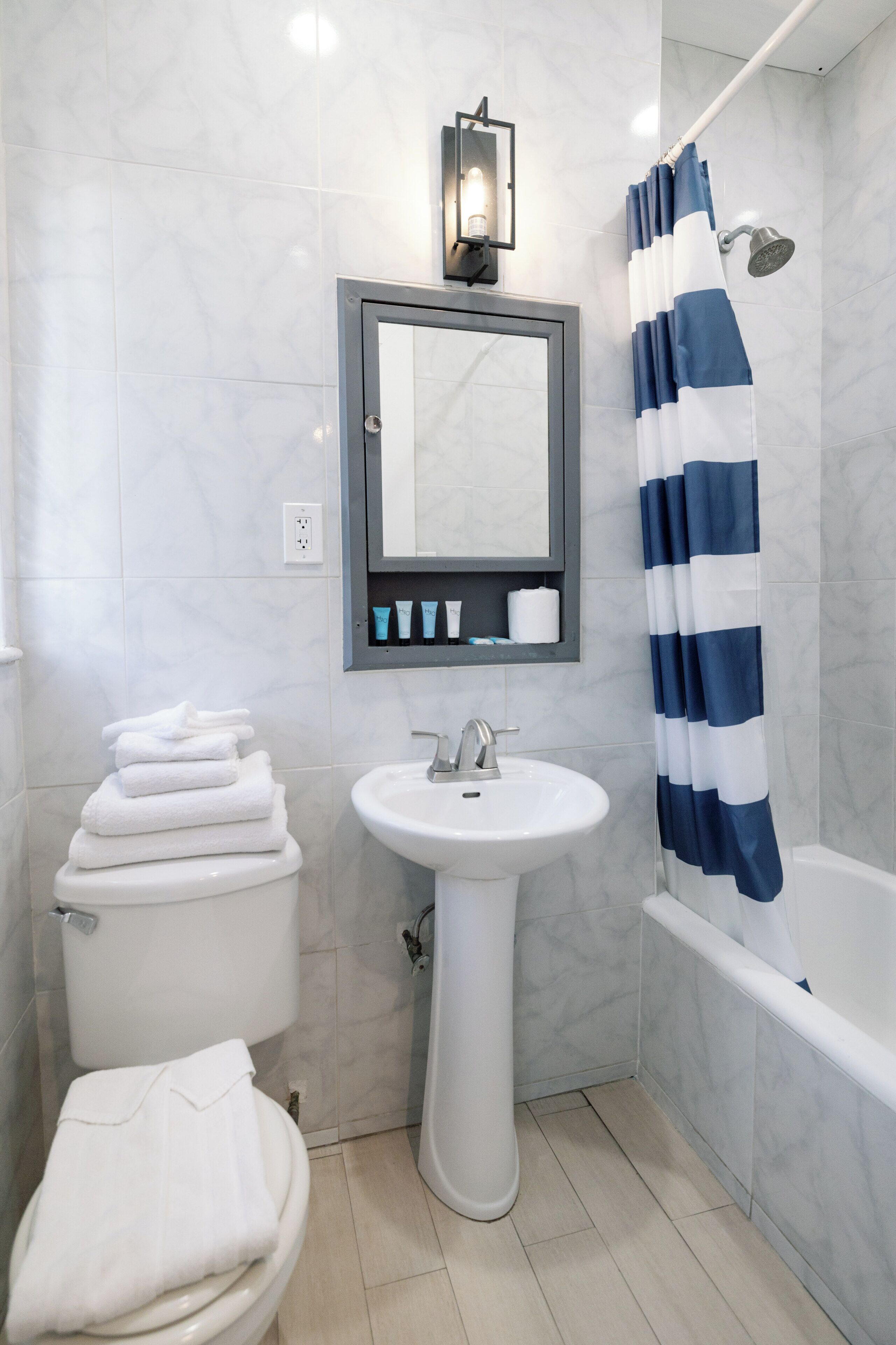 Een badkamer met een wit toilet, een wastafel op een voetstuk, een spiegel boven de wastafel en een douchegordijn met blauwe en witte strepen.