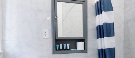 Een badkamer met een wit toilet, een wastafel op een voetstuk, een spiegel boven de wastafel en een douchegordijn met blauwe en witte strepen.