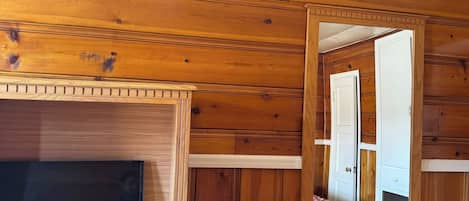 Una habitación con paredes de madera, televisor, espejo y una mesita.