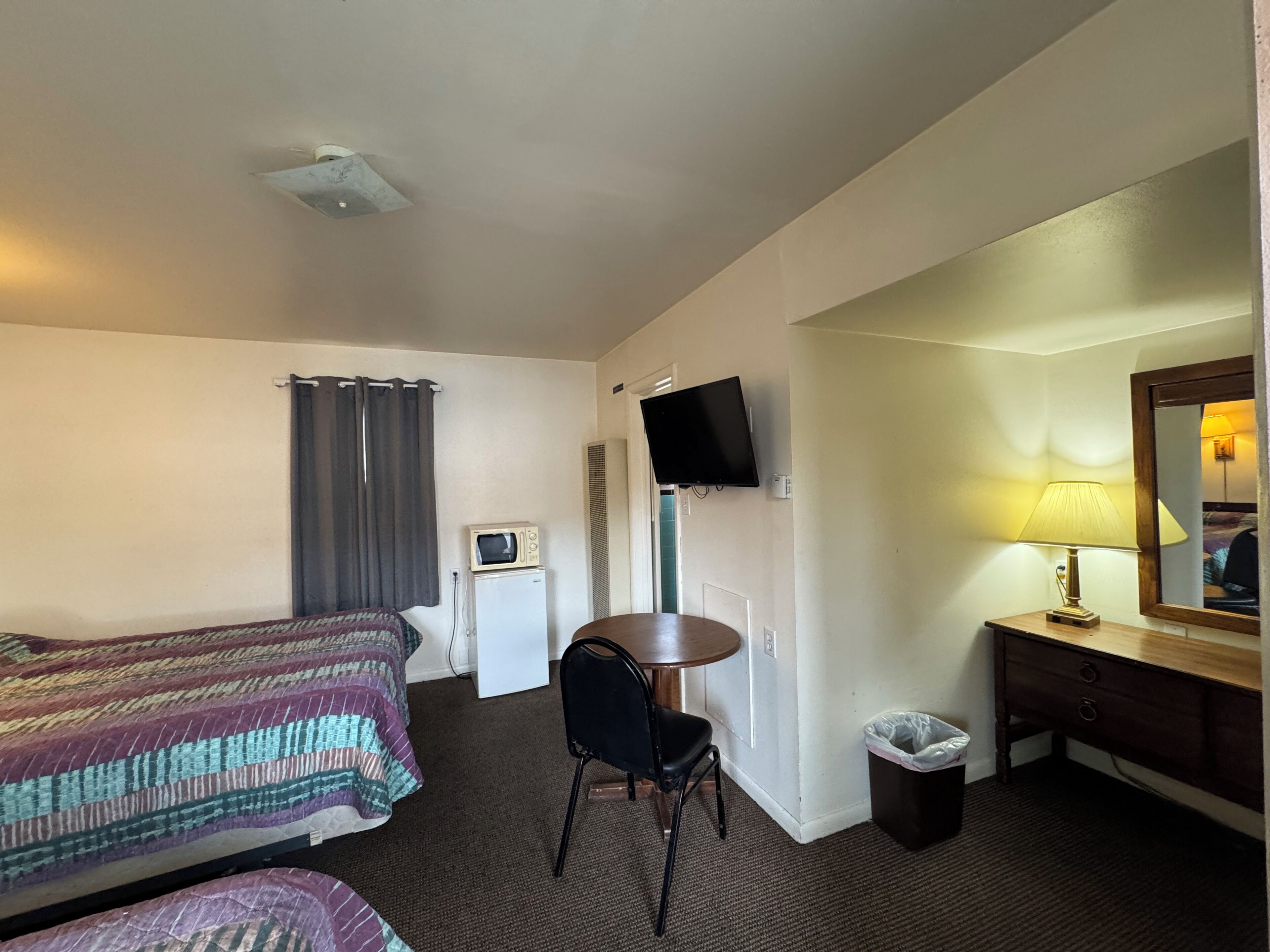 A hotel room with a bed, a desk, a television, a lamp, and a trash bin.