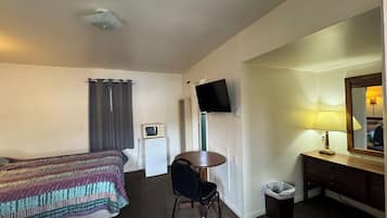 A hotel room with a bed, a desk, a television, a lamp, and a trash bin.
