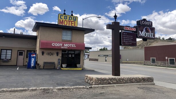 The Cody Motel with a signboard indicating amenities like Wi-Fi, kitchenettes, refrigerators, microwaves, and availability for weekly and monthly stays.
