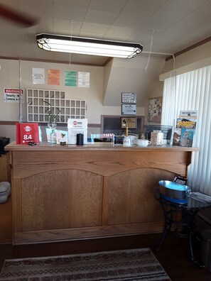 A reception desk with a wooden panel design, a digital screen, and various items like a coffee pot and a sign indicating a 9.4 rating. - Cody Motel Rock Springs WY (Rock Springs)