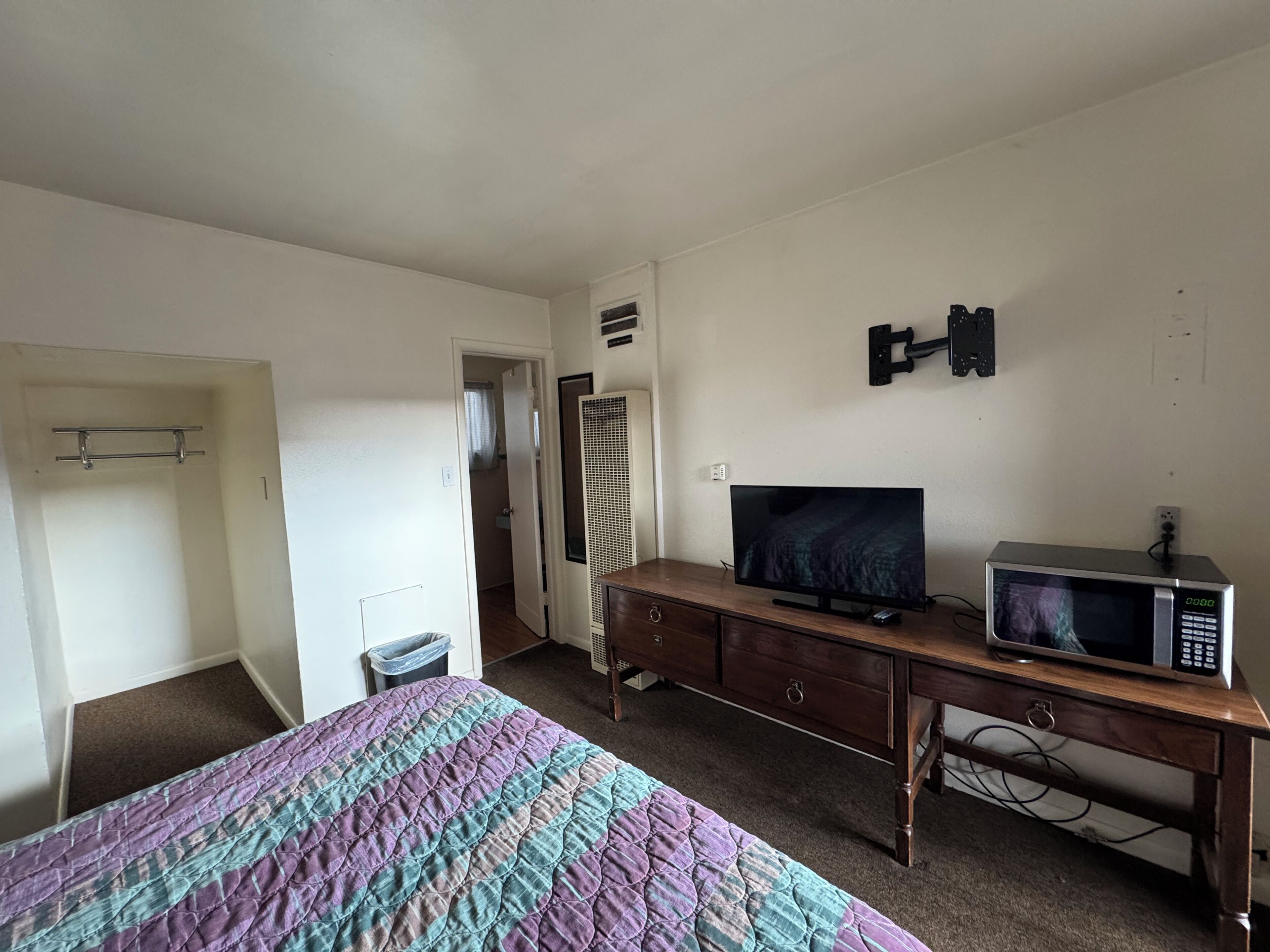 Une chambre à coucher comprenant un lit, une télévision, un four à micro-ondes, une commode et une porte donnant accès à une salle de bain.