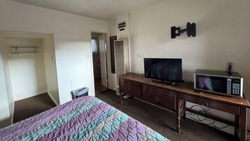A bedroom with a bed, a television, a microwave, a dresser, and a door leading to a bathroom.