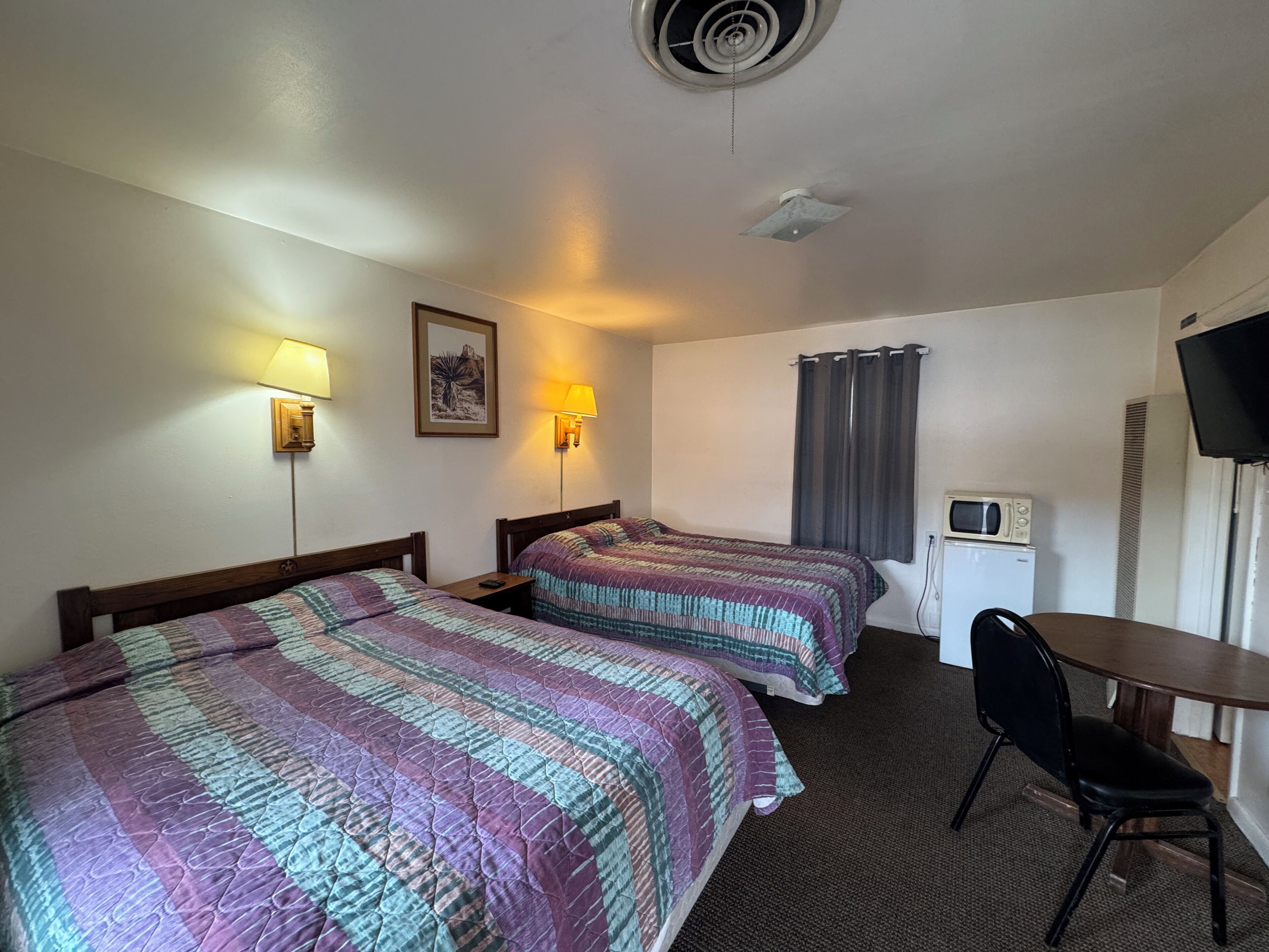 A hotel room with two beds, a desk, a chair, a television, and a microwave.
