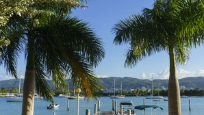 A marina with boats docked, palm trees, and a clear view of mountains in the background. - Seawind On The Bay Beach Condo OLR (Montego Bay)