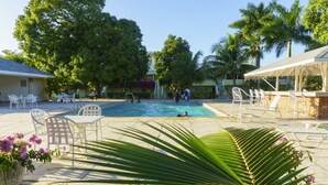 A pool area with chairs and tables, surrounded by palm trees and a building. - Seawind On The Bay Beach Condo OLR (Montego Bay)