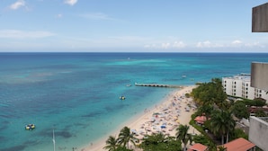 A beach with clear turquoise waters, a pier, and a row of beach umbrellas. - Sunset Beach Studio At Montego Bay Club Resort (Montego Bay)