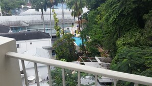 Vista de un hotel con piscina rodeada de abundante vegetación, un área al aire libre techada y un edificio con techo plano.