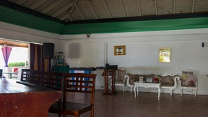 Una habitación amplia con techo alto, una mesa de madera, sillas, un sofá y una mesita con un ordenador portátil.