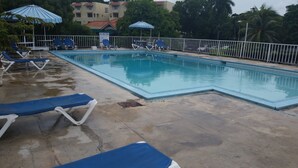 Una piscina con agua azul, rodeada por una cerca blanca y varias sillas de descanso azules.