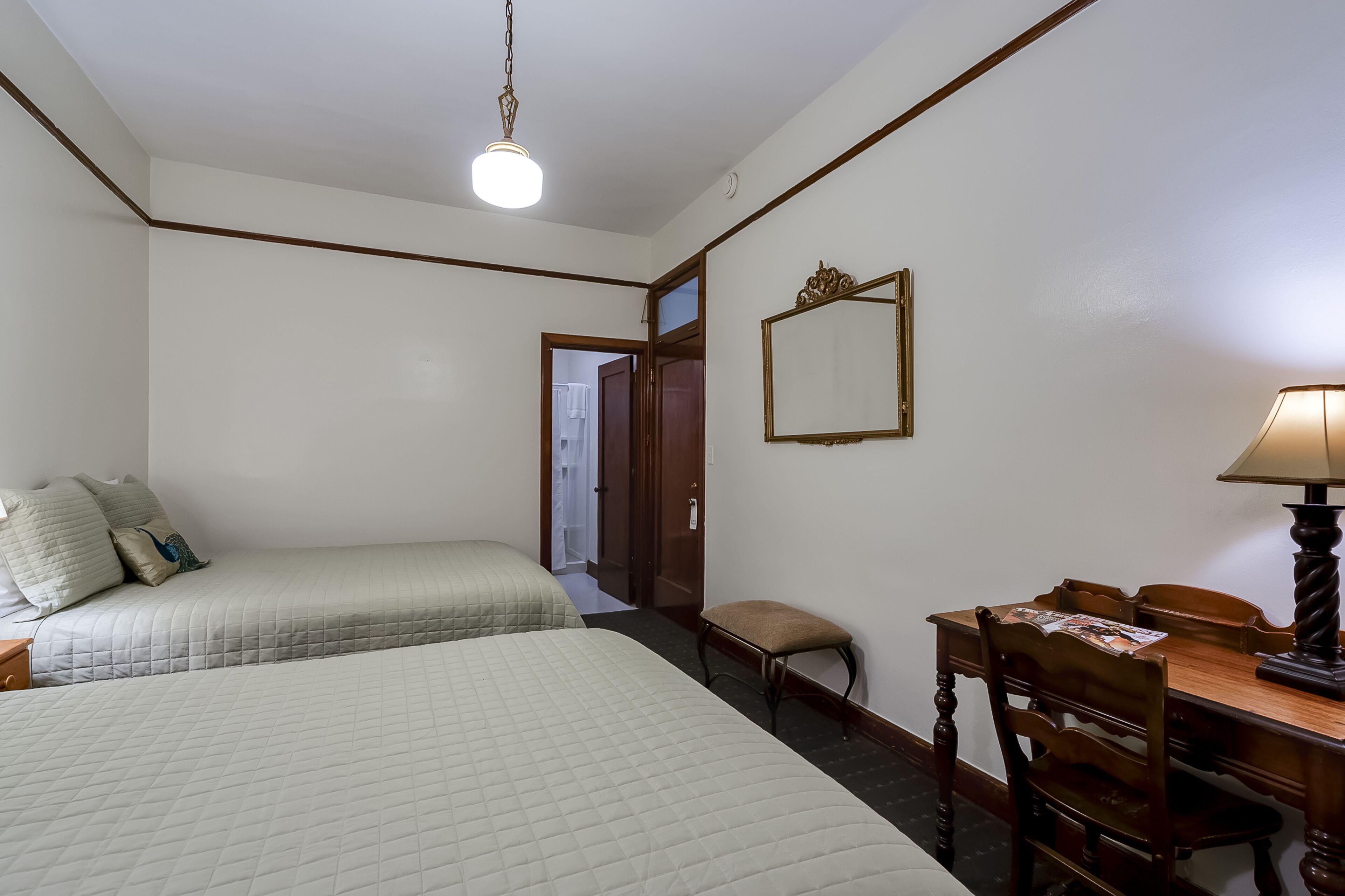 Habitación de hotel con dos camas, un escritorio con silla, una lámpara y un espejo en la pared.
