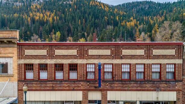 A two-story brick building with a 'RYAN BUILDING' sign, a 'Little Hair House Salon' on the ground floor, and a mountain backdrop. - Ryan Hotel (Wallace)
