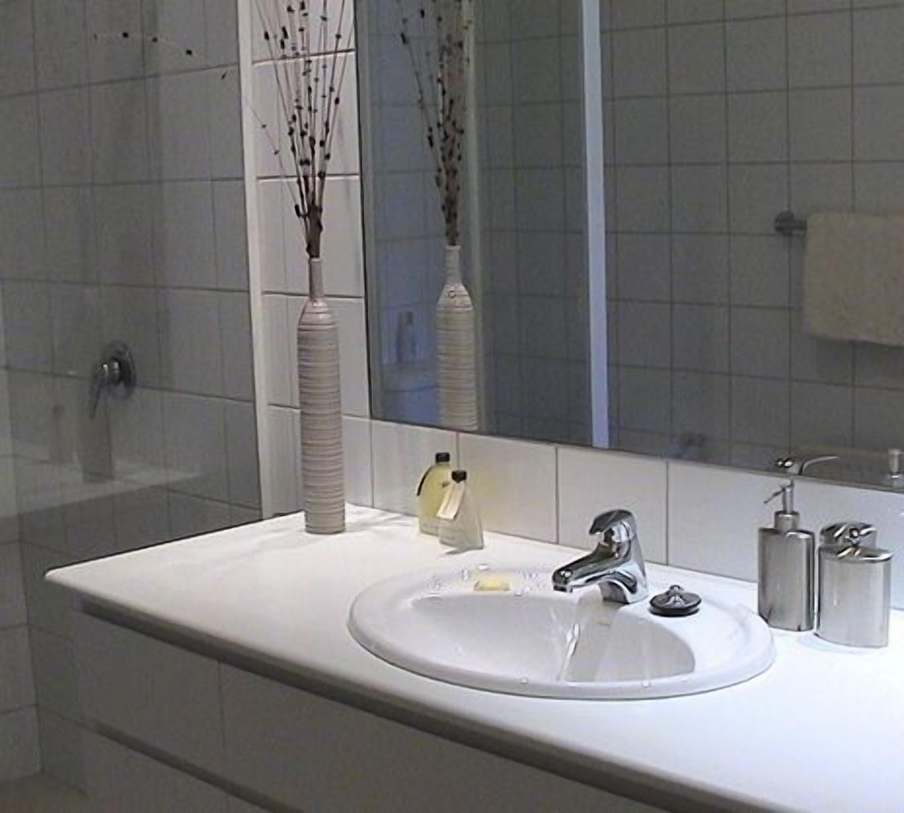 A bathroom with a white sink, a mirror, and a vase with branches.