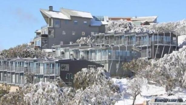 Un edificio moderno con varios niveles y grandes ventanales, rodeado de árboles cubiertos de nieve.