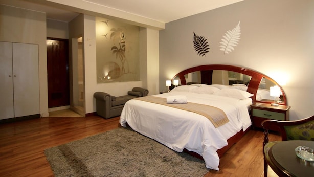 A hotel room with a large bed, a desk, a chair, a wardrobe, and a wall with a fern decoration. - Hotel Pacifico Miraflores (Lima)