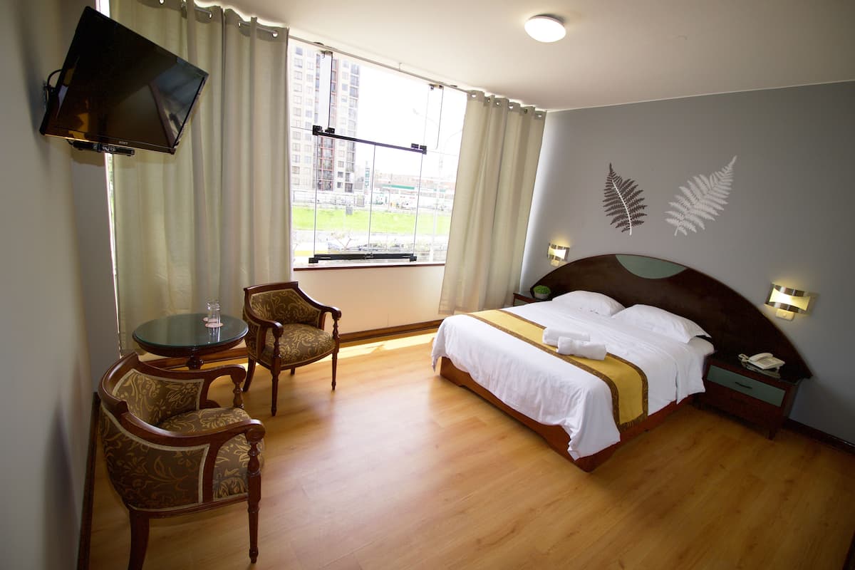 Habitació d'hotel amb un llit, una televisió penjada a la paret, una taula de treball amb una cadira i una finestra amb cortines.