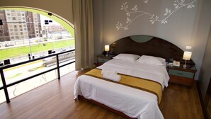 A hotel room with a large bed, two bedside tables, a view of a building and a road through a large window, and a decorative wall design. - Hotel Pacifico Miraflores (Lima)