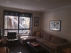 A living room with a large window, a sofa, a coffee table, and a television. - Peak 105 (Mount Buller)