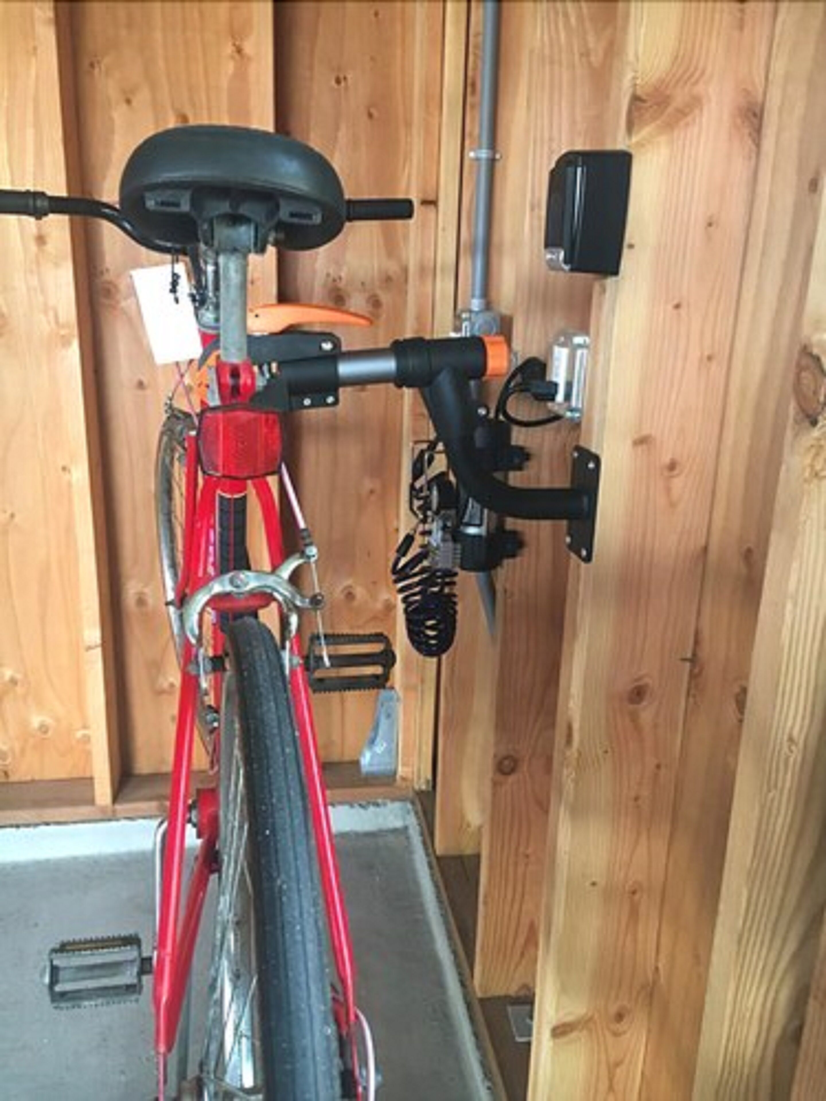 A red bicycle parked inside a wooden structure with a metal railing and a black object on the wall.
