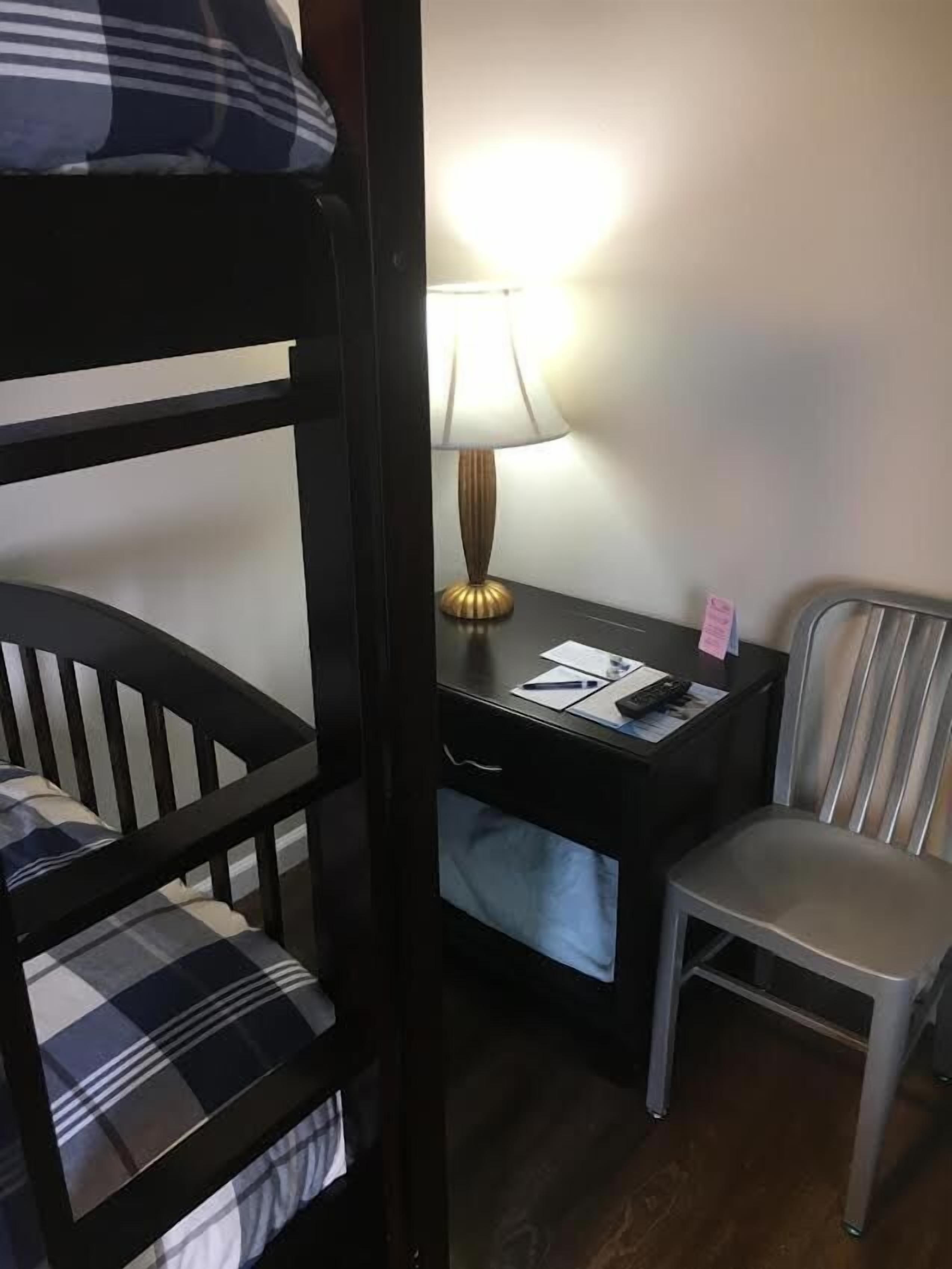 A bunk bed with a checkered pillow, a desk with a lamp, and a chair.
