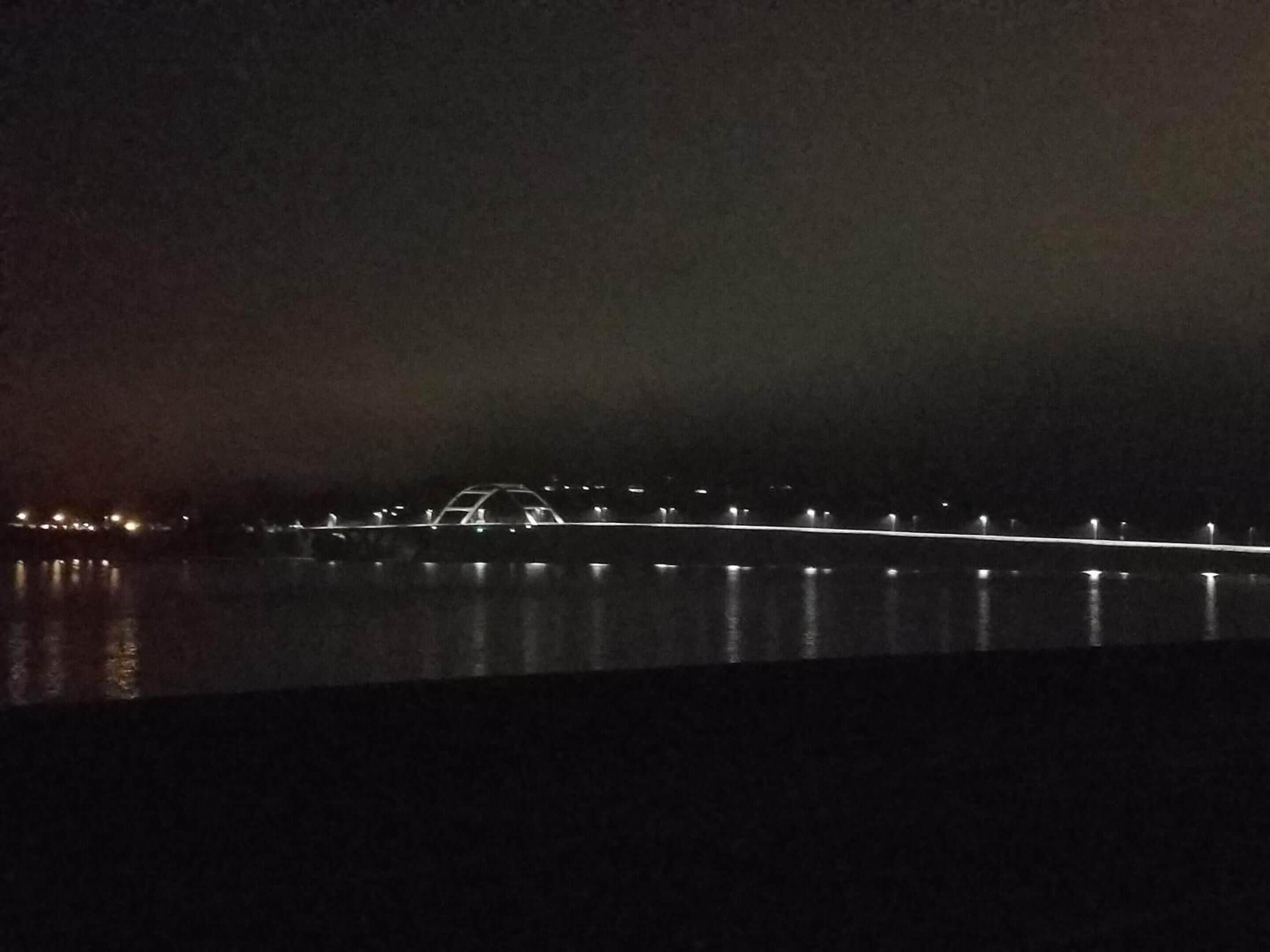 A nighttime view of a bridge with lights reflecting on the water.