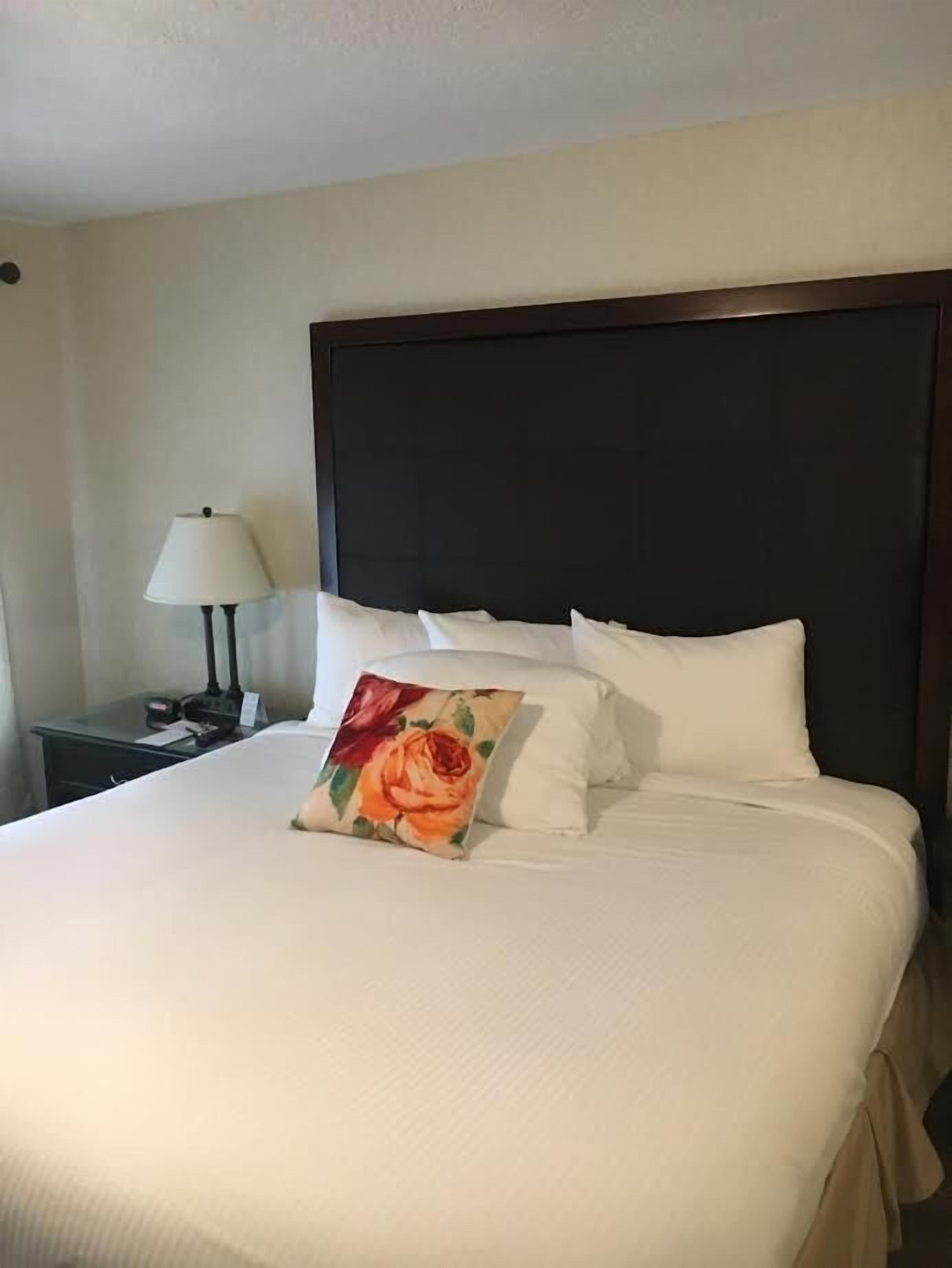 A neatly made bed with white bedding and a single decorative pillow featuring a rose.