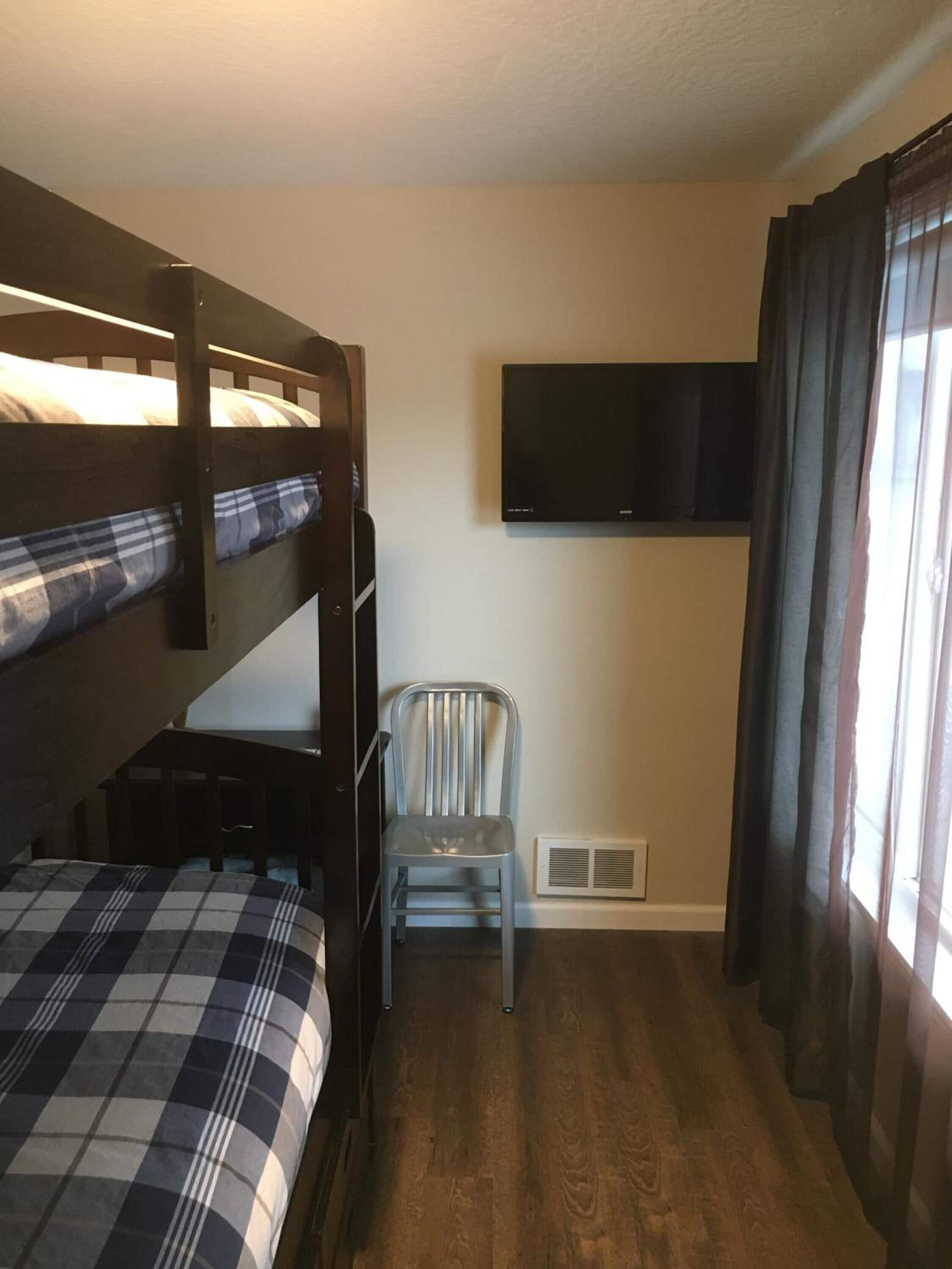 A bunk bed room with a television mounted on the wall and a chair.
