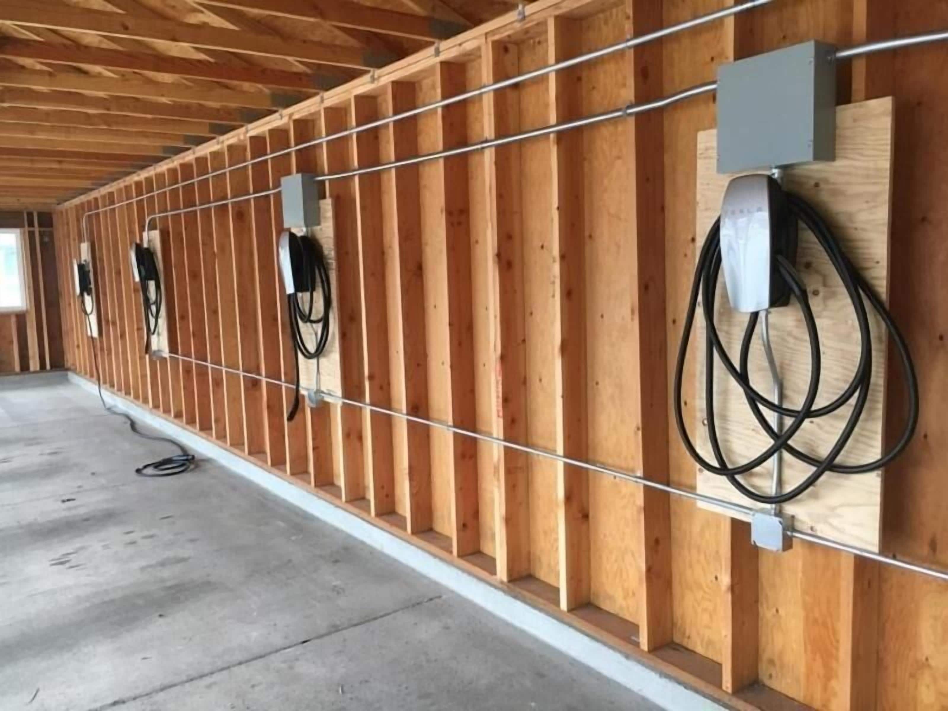 A room with wooden walls and a concrete floor, featuring electrical outlets and cables.