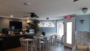 A dining area with a bar, wooden flooring, a ceiling fan, and a patterned armchair. - The Waldport Inn (Waldport)