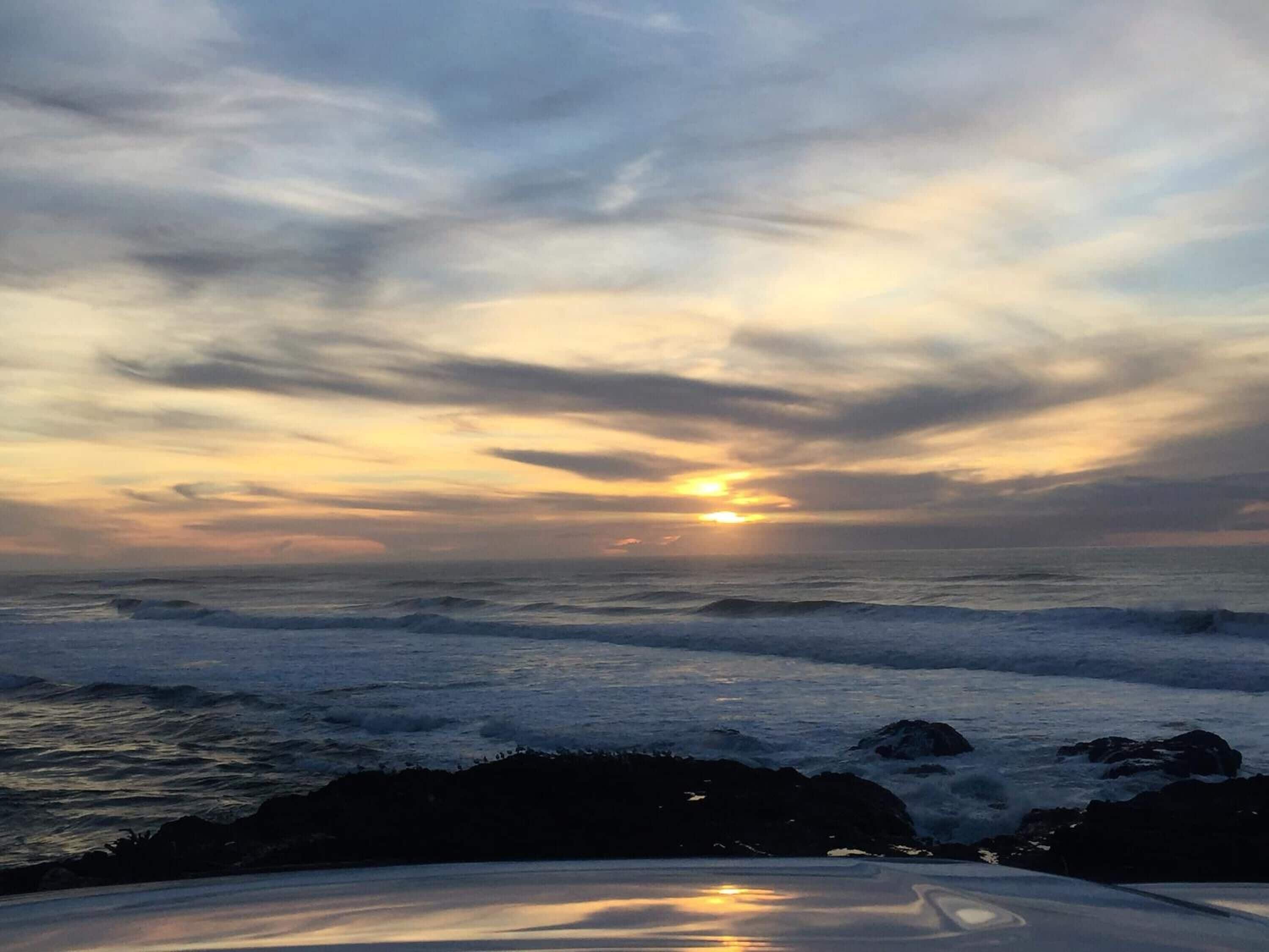 A sunset over the ocean with waves crashing onto rocks.
