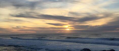 A sunset over the ocean with waves crashing onto rocks.