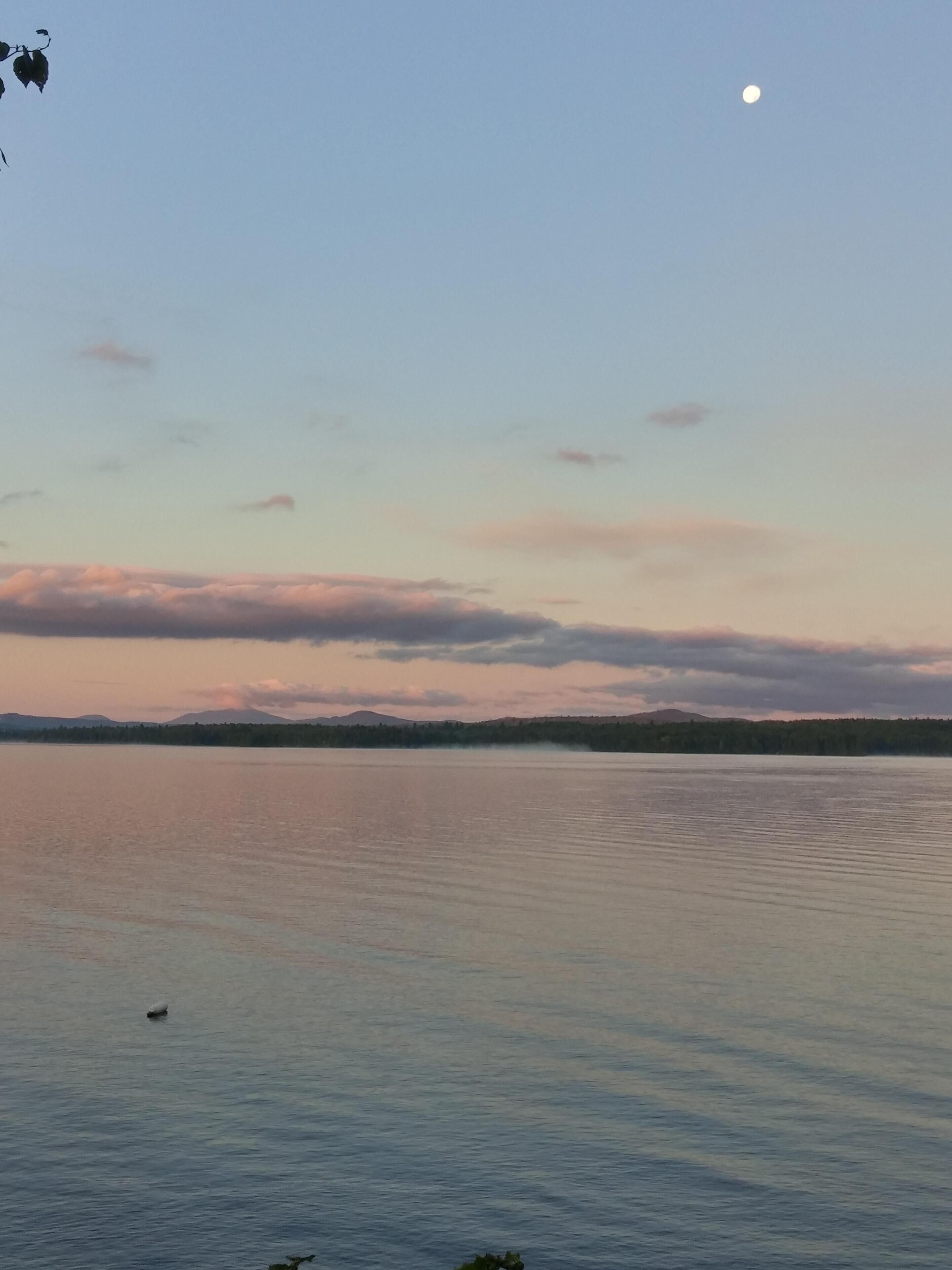 A calm lake with a clear sky and a visible moon.